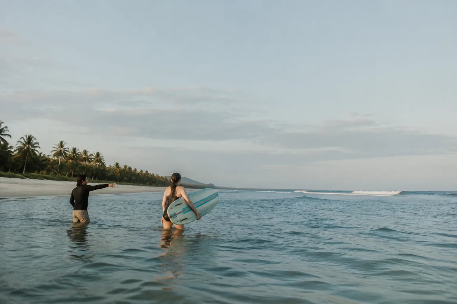 A coach guiding a learner in shallow water at a quiet Indonesian beach