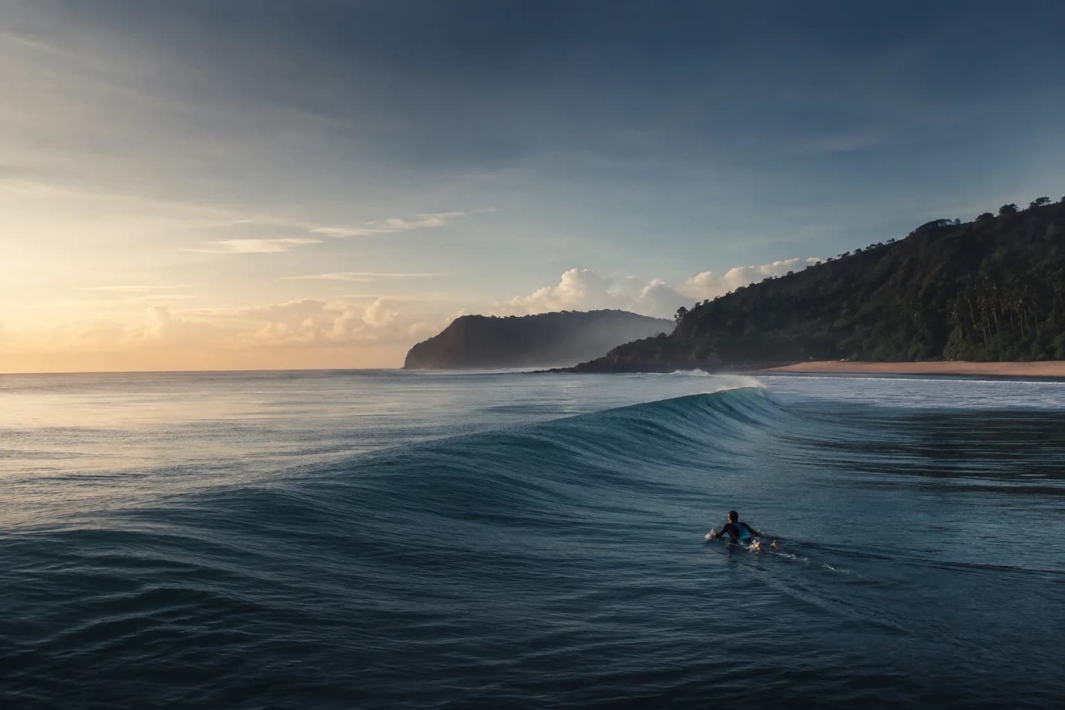 A lone surfer paddling beyond a calm Indonesian swell at dawn