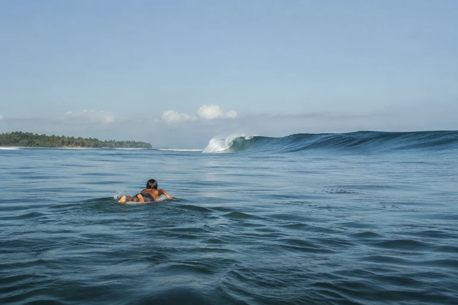 A surfer paddling toward a modest tropical reef shoulder