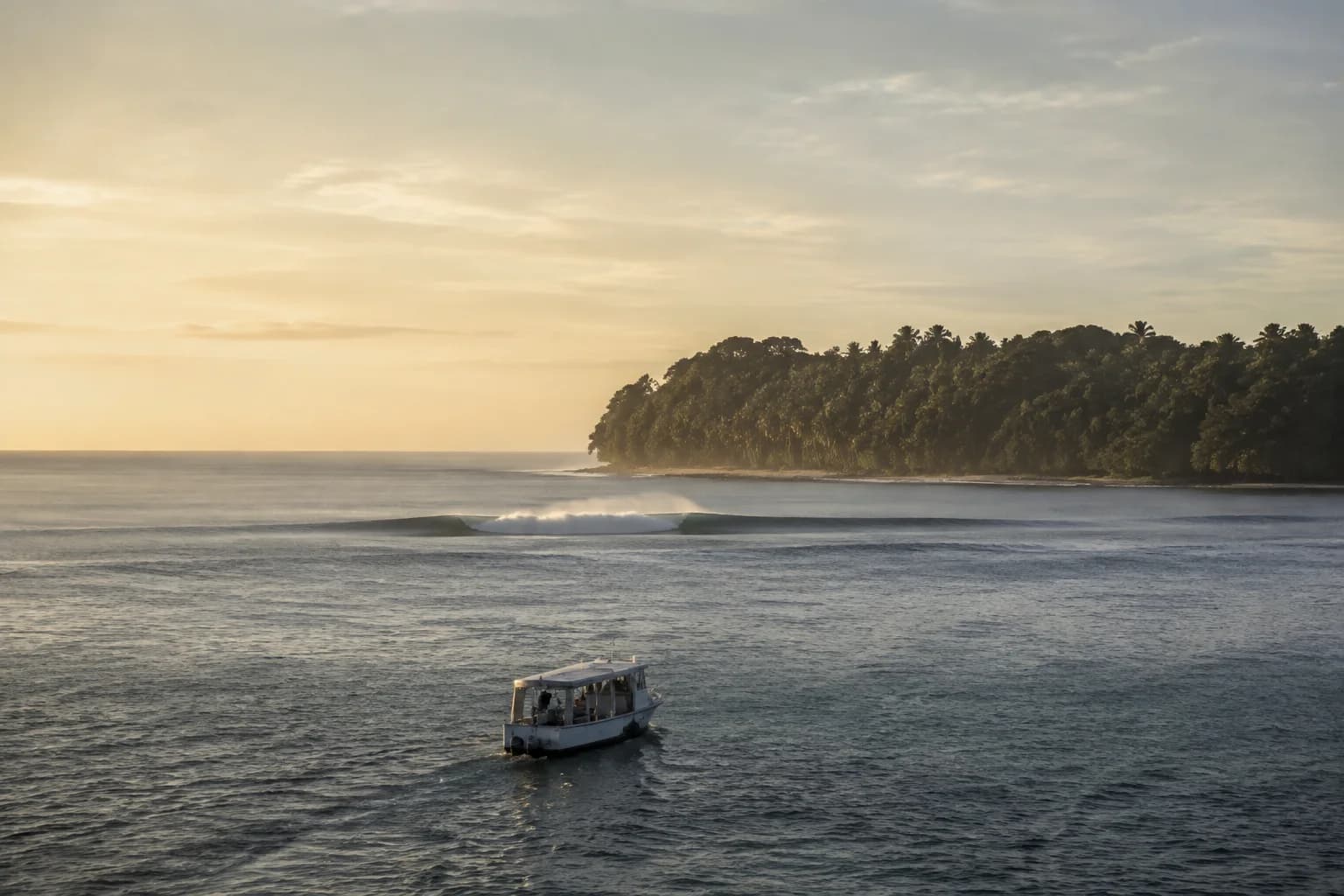 A small surf charter approaching a remote forested Indonesian reef island